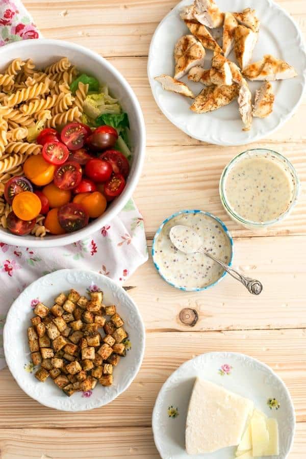 ingredients for chicken caesar pasta salad on a wooden board