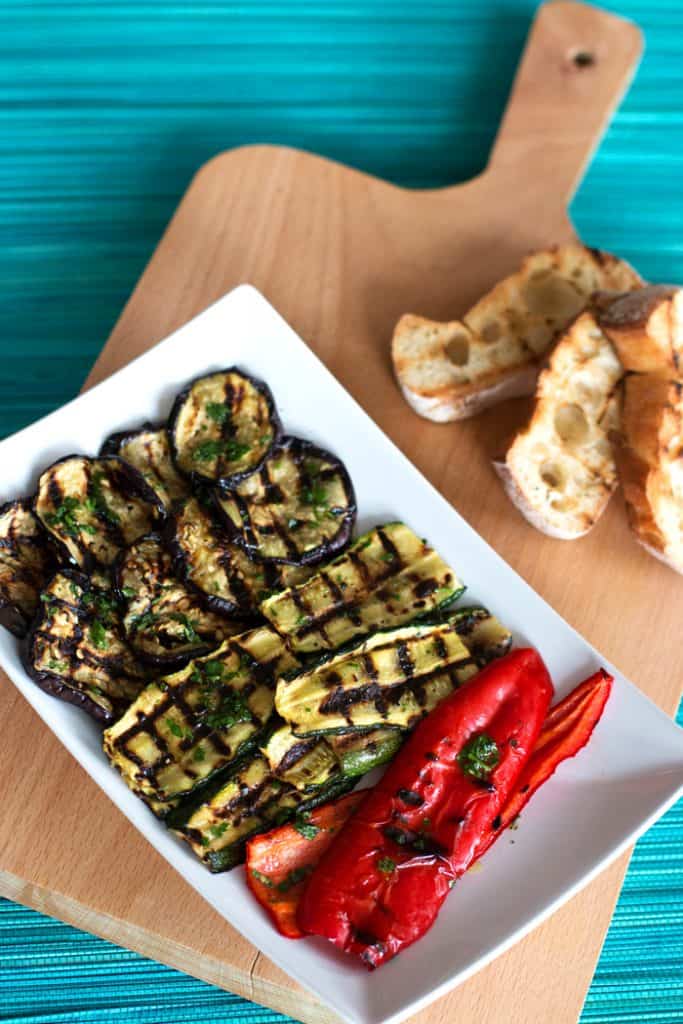 wooden board on blue mat with plate filled with grilled vegetables