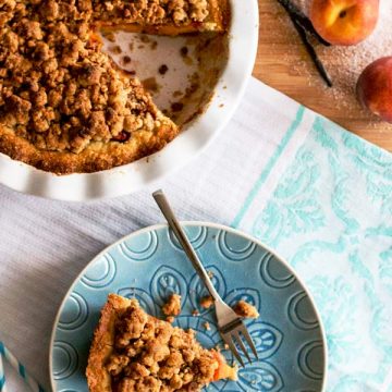 top down view on slice of peach pie on a blue plate next to peach pie