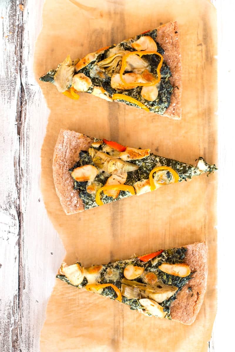 three slices of spinach artichoke pizza on a piece of baking parchment