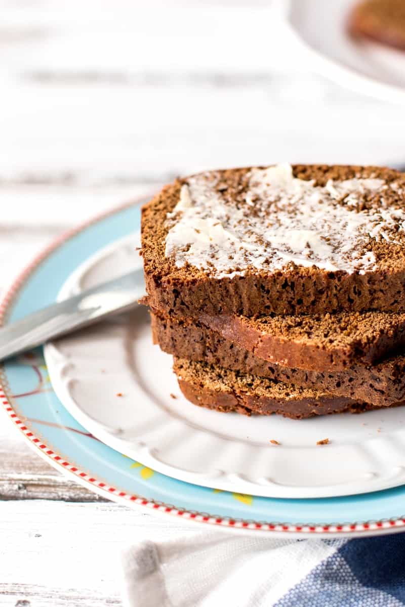 stack of sliced Dutch honey bread on a plate, top slice spread with butter 