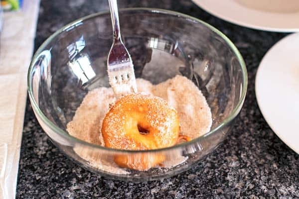 tossing an apple fritter in cinnamon sugar with a fork