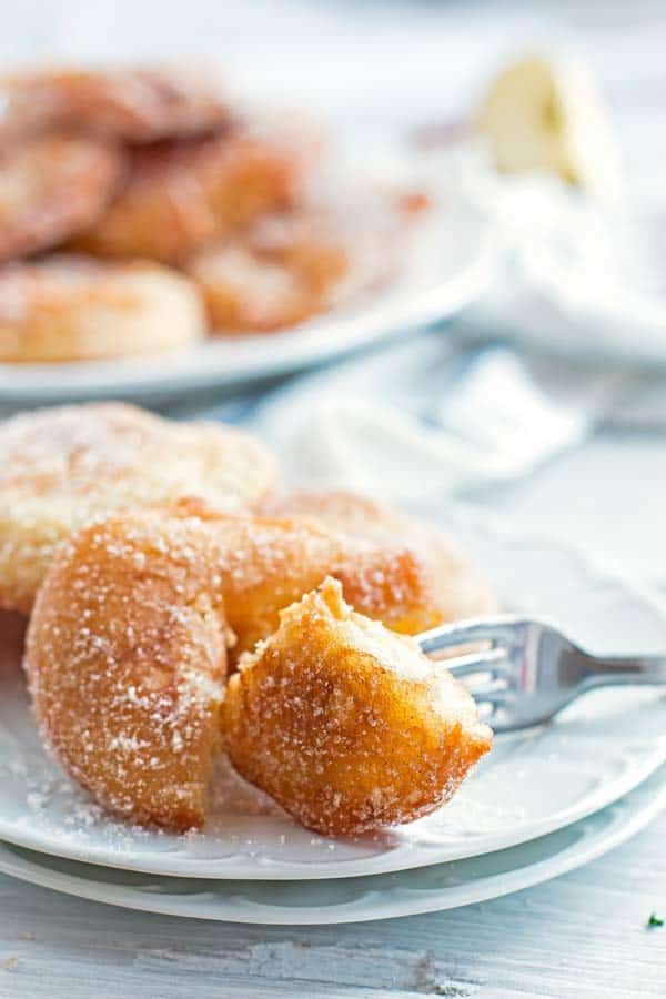 apple fritter on a plate with a fork and a pile of fritters in the background