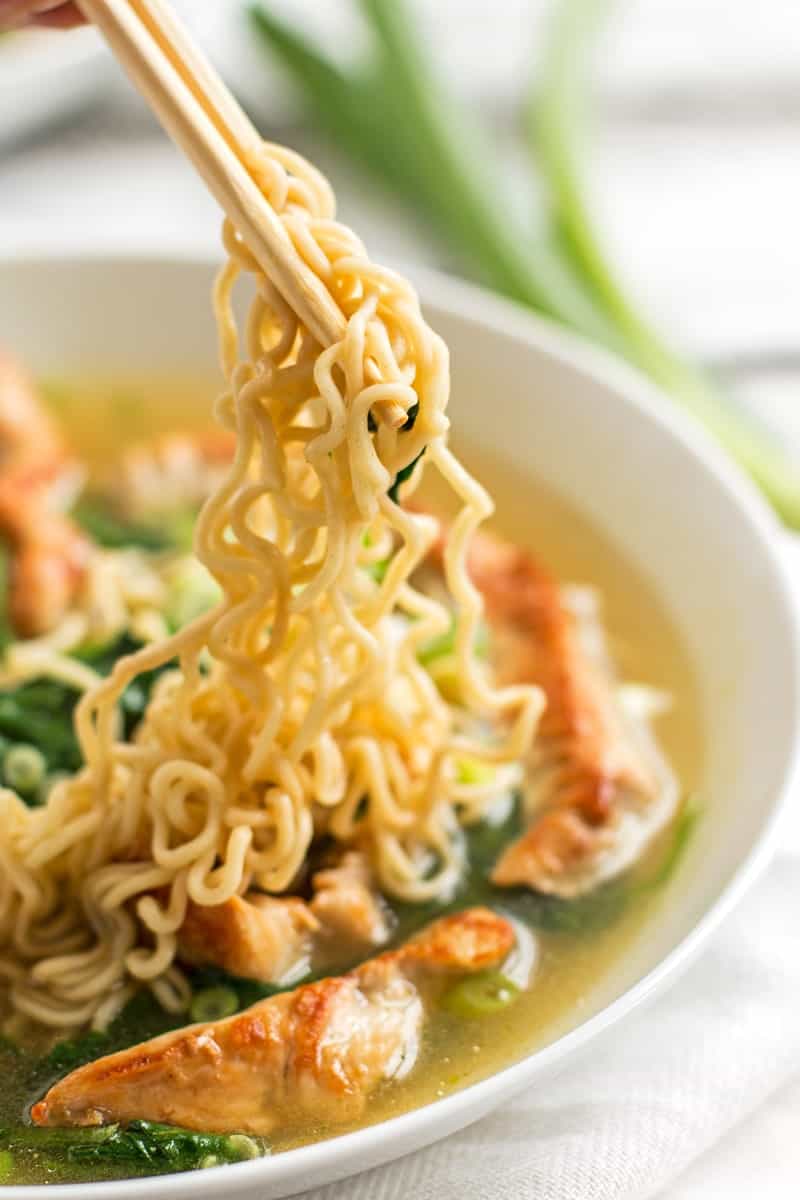 chopsticks holding Ramen noodles over a bowl of soup