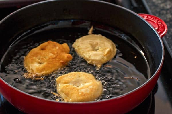 three apple fritters floating in hot oil in a cast iron skillet