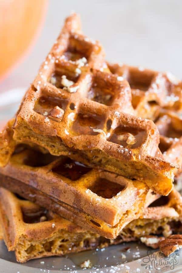 stack of pumpkin waffles sprinkled with pecans and drizzled with syrup