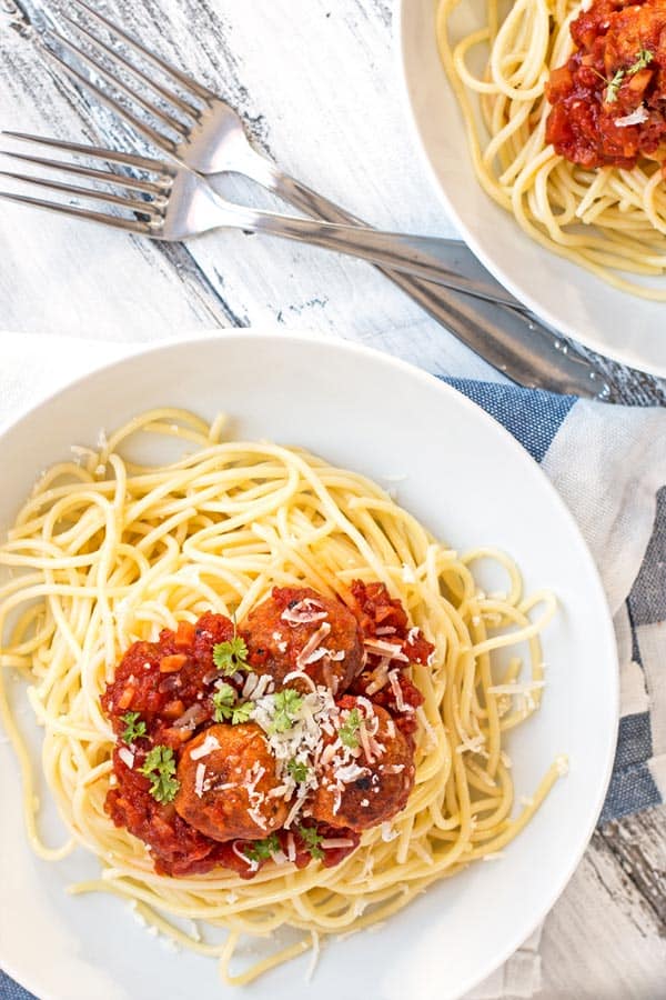 two white plates with forks, filled with spaghetti, tomato sauce and turkey meatballs