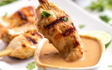 female hand dipping grilled chicken in peanut sauce