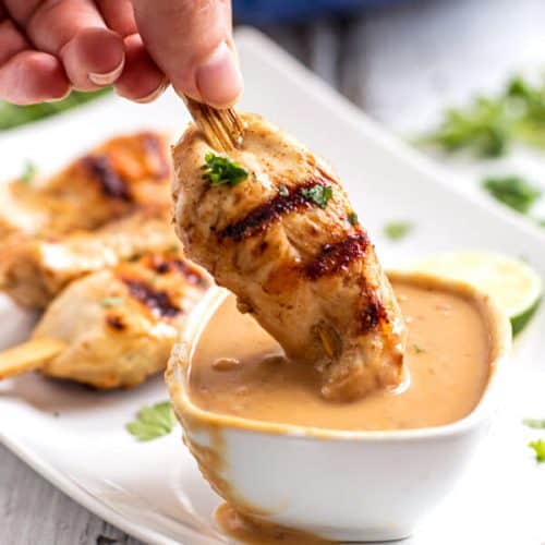 female hand dipping grilled chicken in peanut sauce