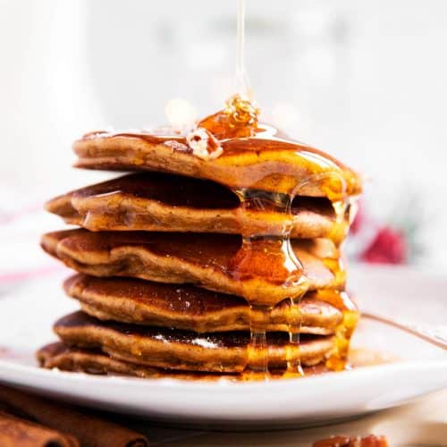 stack of gingerbread pancakes with maple syrup drizzling over