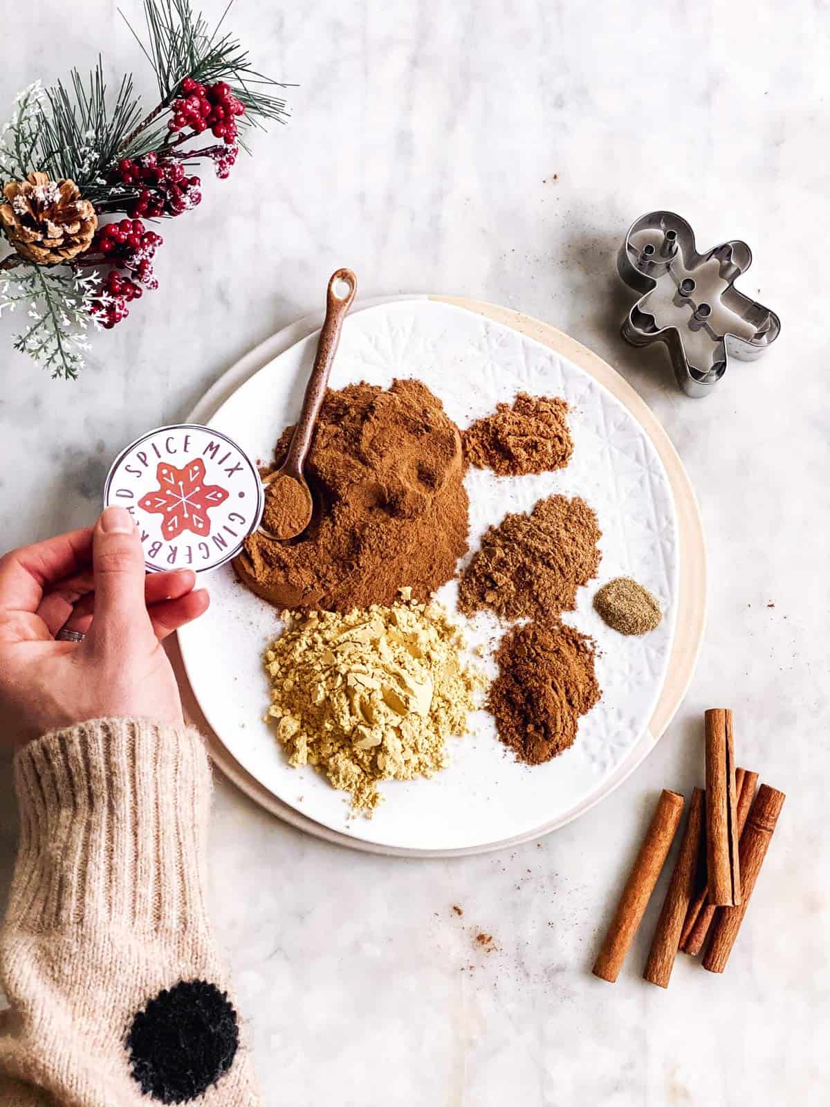 plate with ingredients for gingerbread spice mix with a female hand holding a gift label next to it