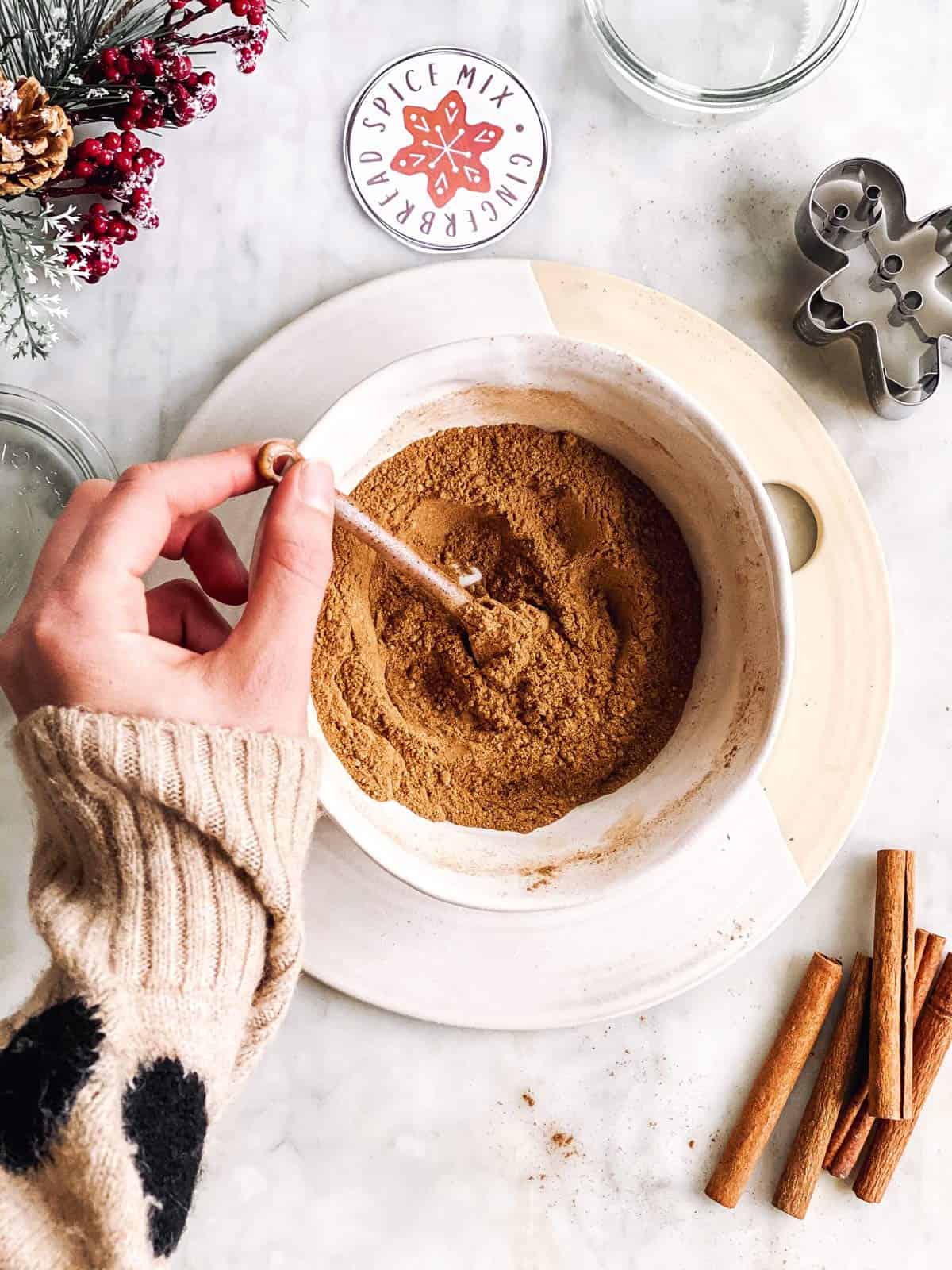 female hand stirring spices to make gingerbread spice mix in a white bowl