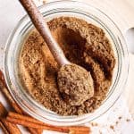 overhead view of gingerbread spice mix in small glass jar with a brown ceramic spoon