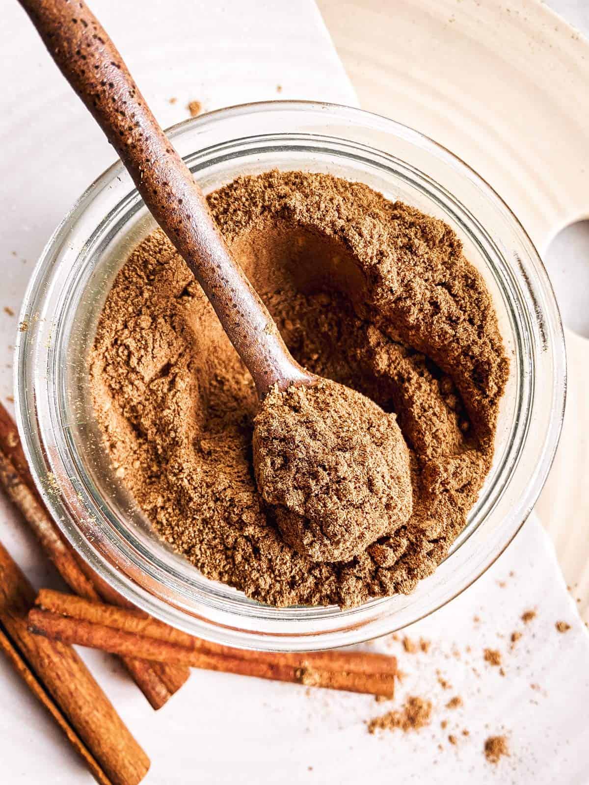 overhead view of gingerbread spice mix in small glass jar with a brown ceramic spoon