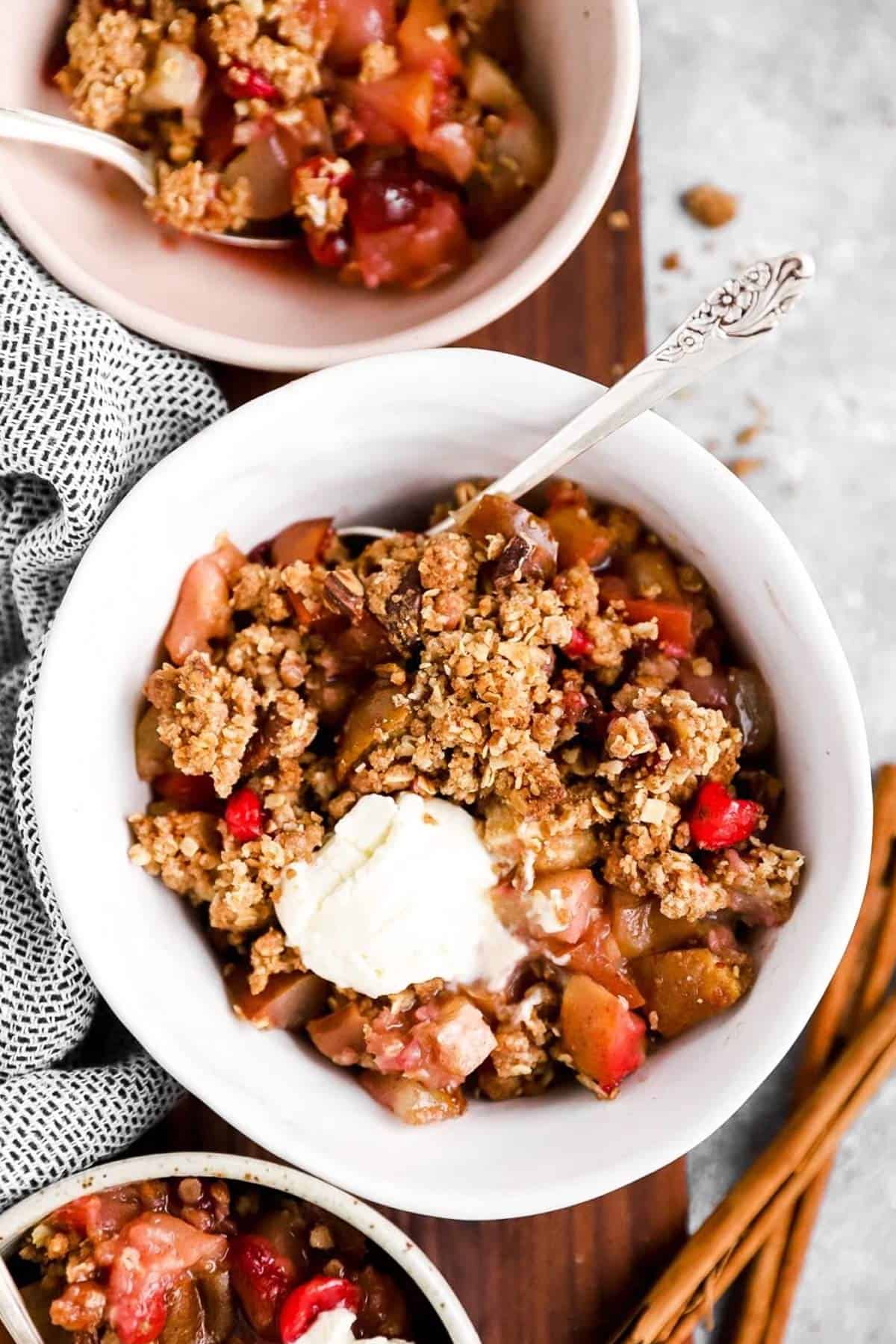 top down view on three bowls filled with fruit crisp and ice cream on a wooden board