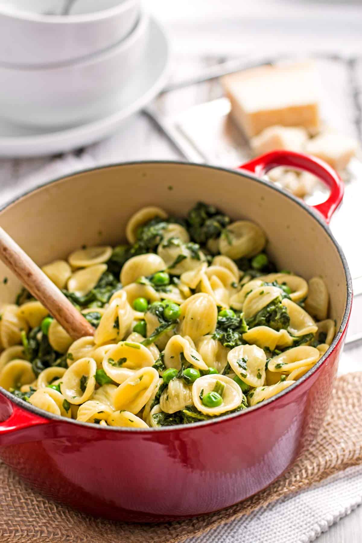 frontal view on red Dutch oven filled with pasta, spinach and peas