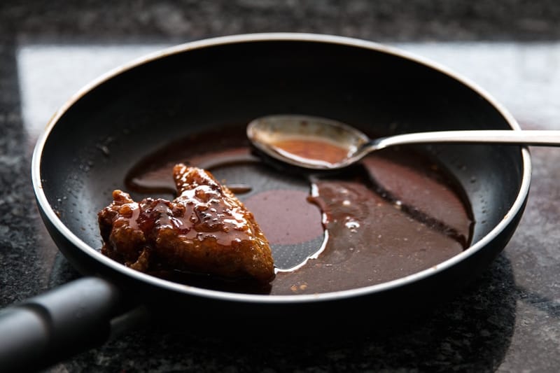 frontal view of skillet with chili sauce, spoon and single chicken wing