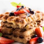 stack of french toast waffles topped with fresh berries and drizzled with maple syrup