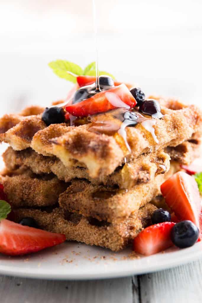 stack of french toast waffles topped with fresh berries and drizzled with maple syrup