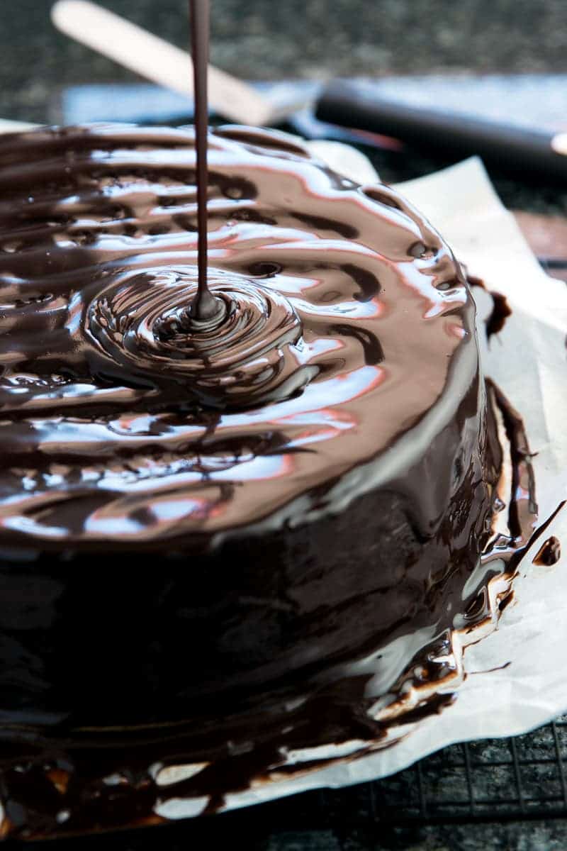 close up view of chocolate glaze drizzling over chocolate cake
