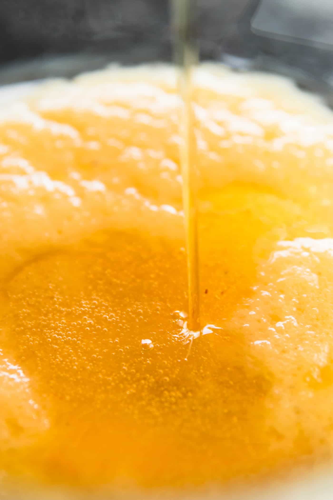 close up photo of honey pouring into bowl with wet ingredients for muffins