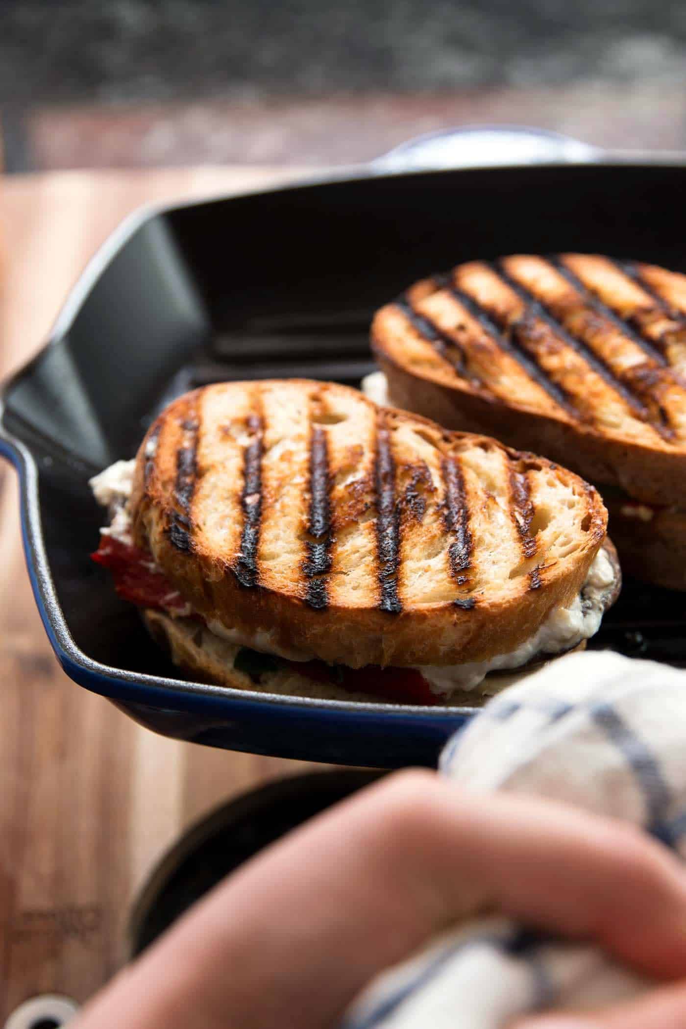 female hand holding a grill pan with two grilled cheese sandwiches inside