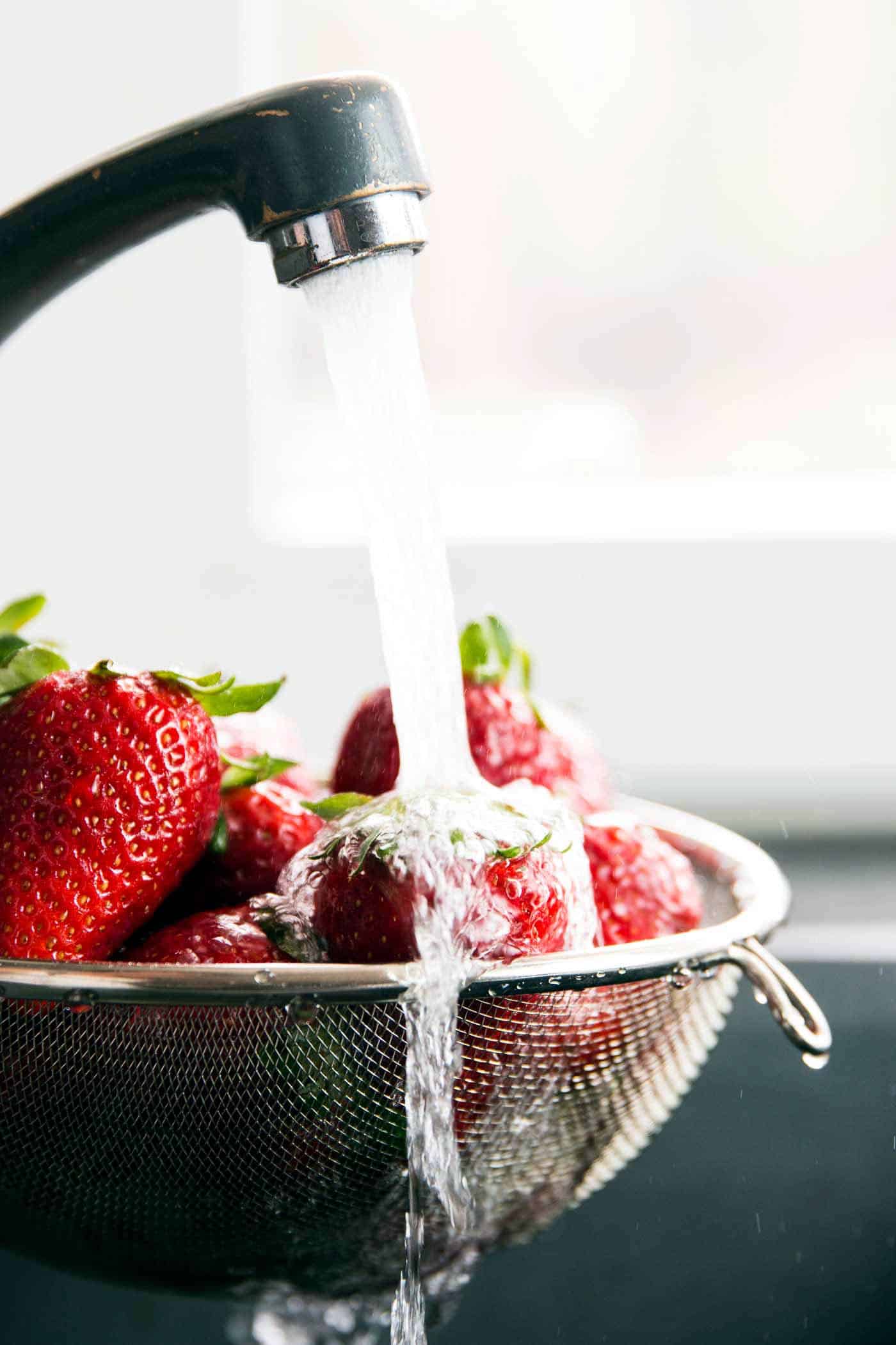 strawberries in a sieve being rinsed under tap water