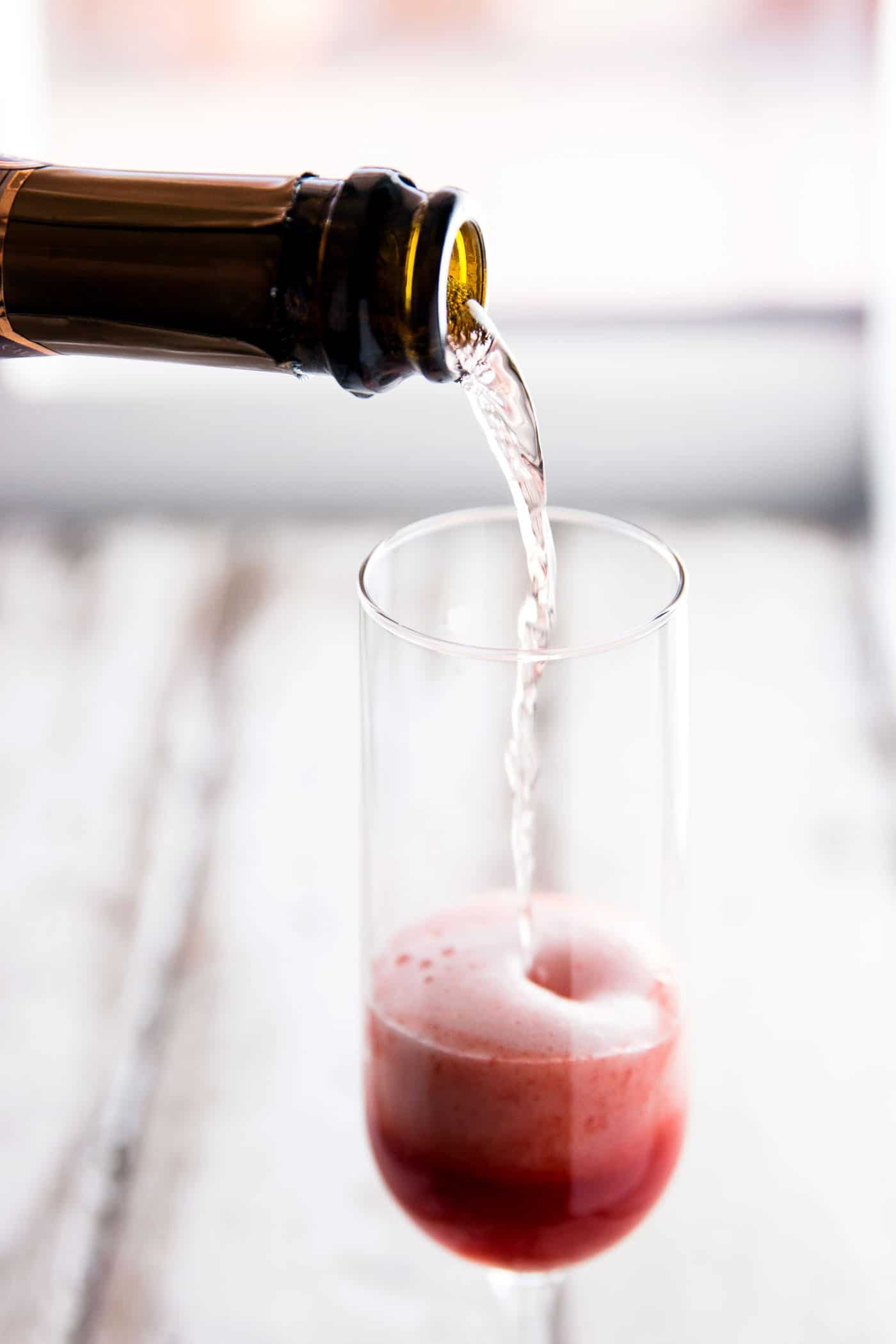 champagne pouring into flute glass over strawberry purée