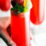 female hand grabbing champagne glass filled with strawberry cocktail