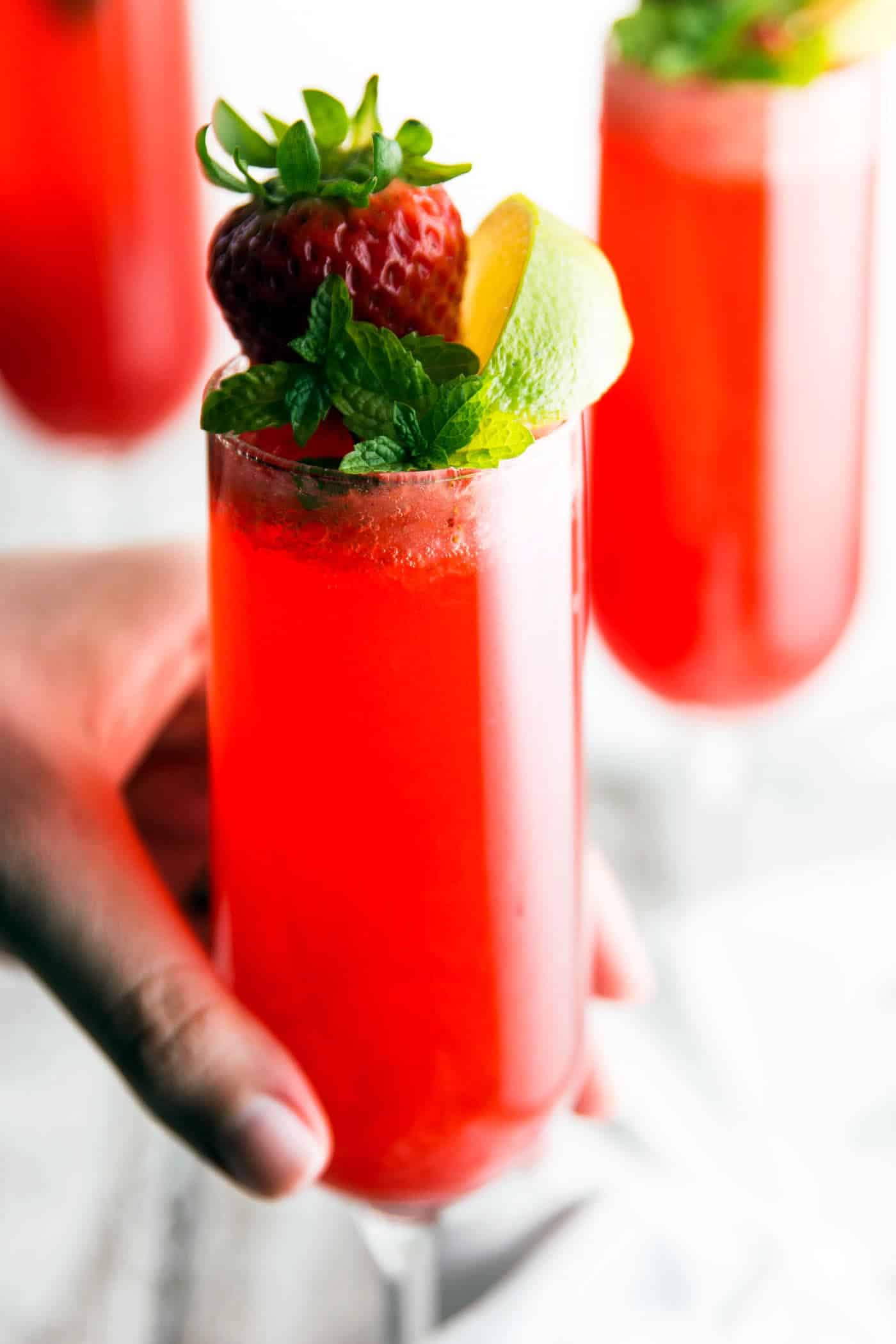 female hand grabbing champagne glass filled with strawberry cocktail