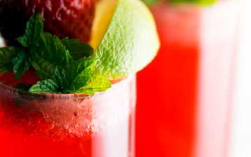 close up photo of champagne glasses filled with strawberry cocktail and garnished with lime, mint and fresh strawberry