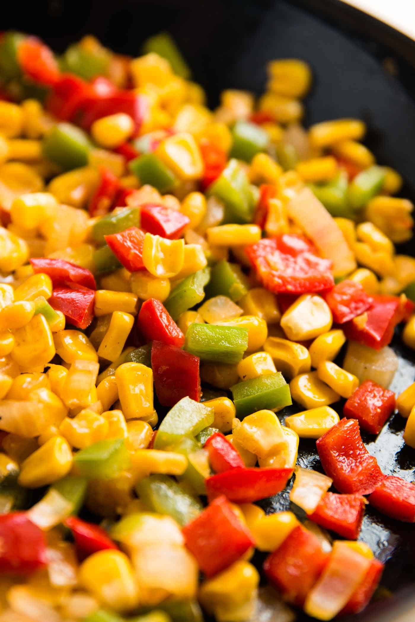 close up photo of diced peppers, onions and corn in skillet