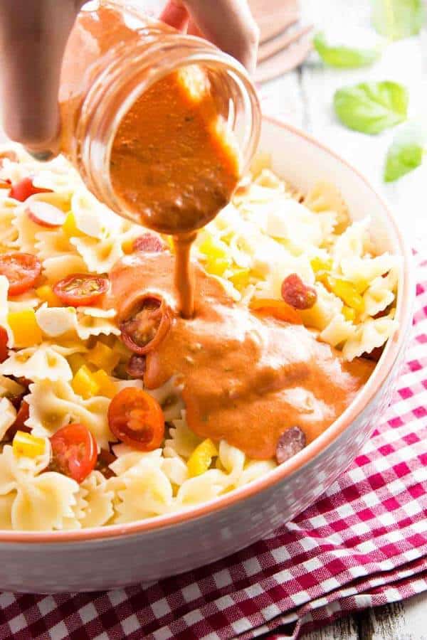 female hand pouring creamy dressing over pasta salad