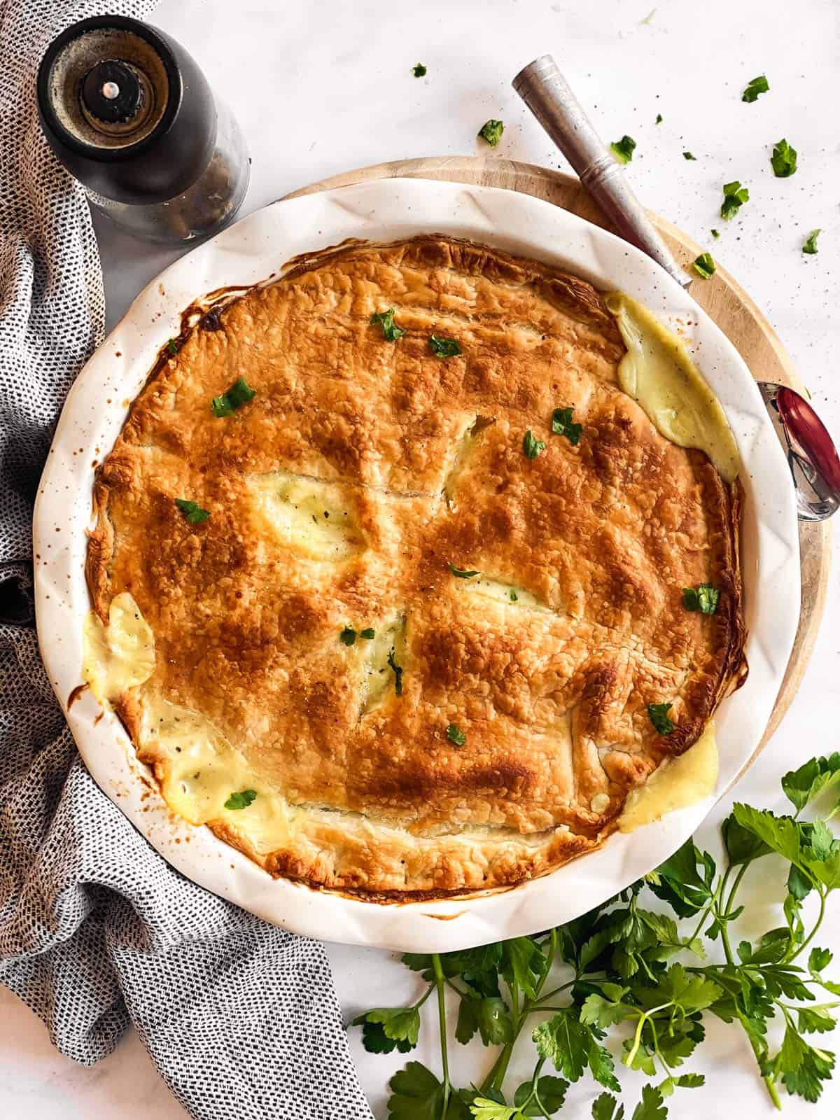 overhead view of baked turkey pot pie on a light surface surrounded by parsley and kitchen tools