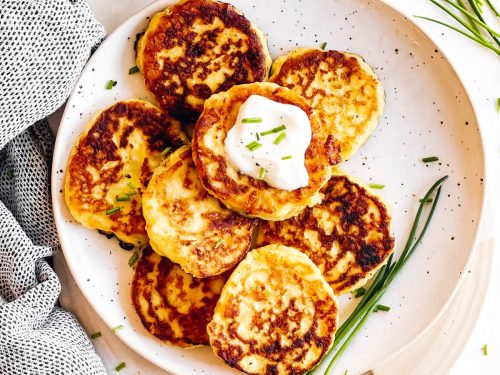 overhead view of potato pancakes on white plate with sour cream