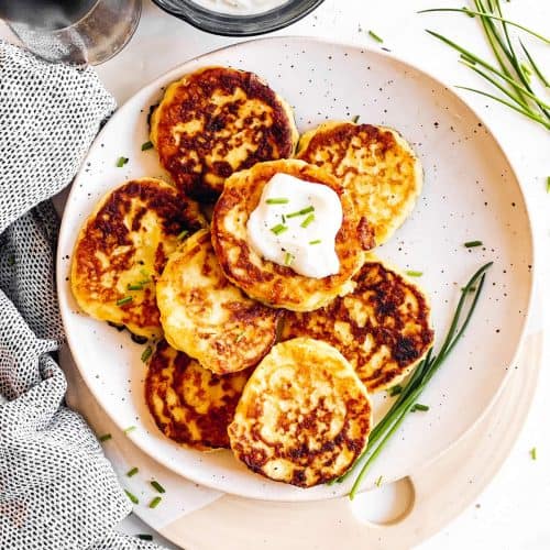 overhead view of potato pancakes on white plate with sour cream