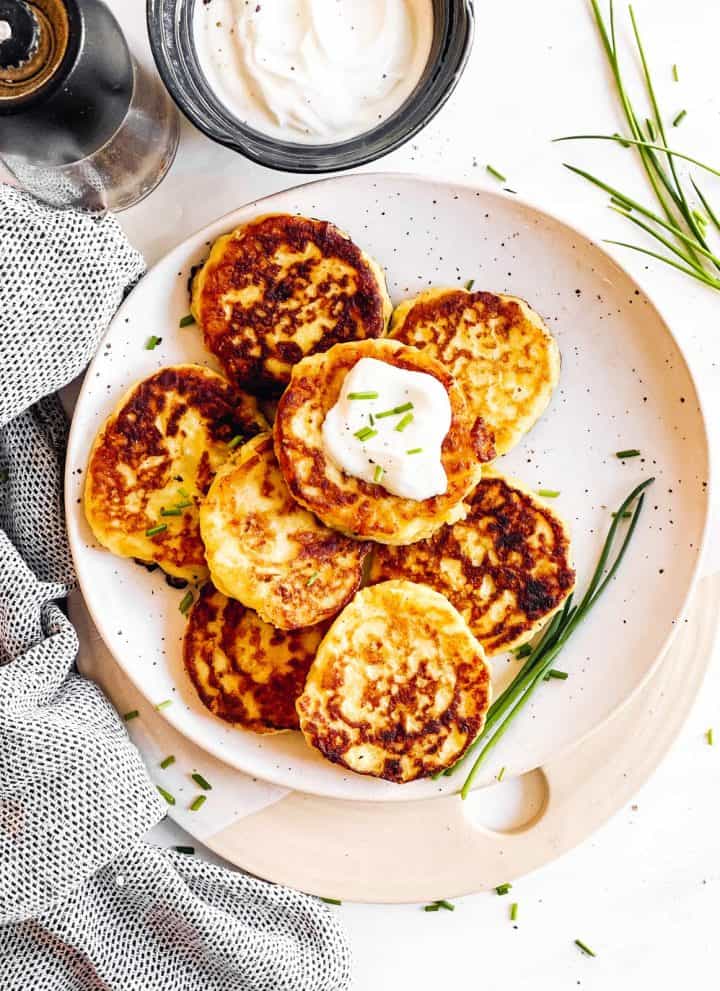overhead view of potato pancakes on white plate with sour cream