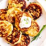 overhead close up view of potato pancakes on white plate with sour cream