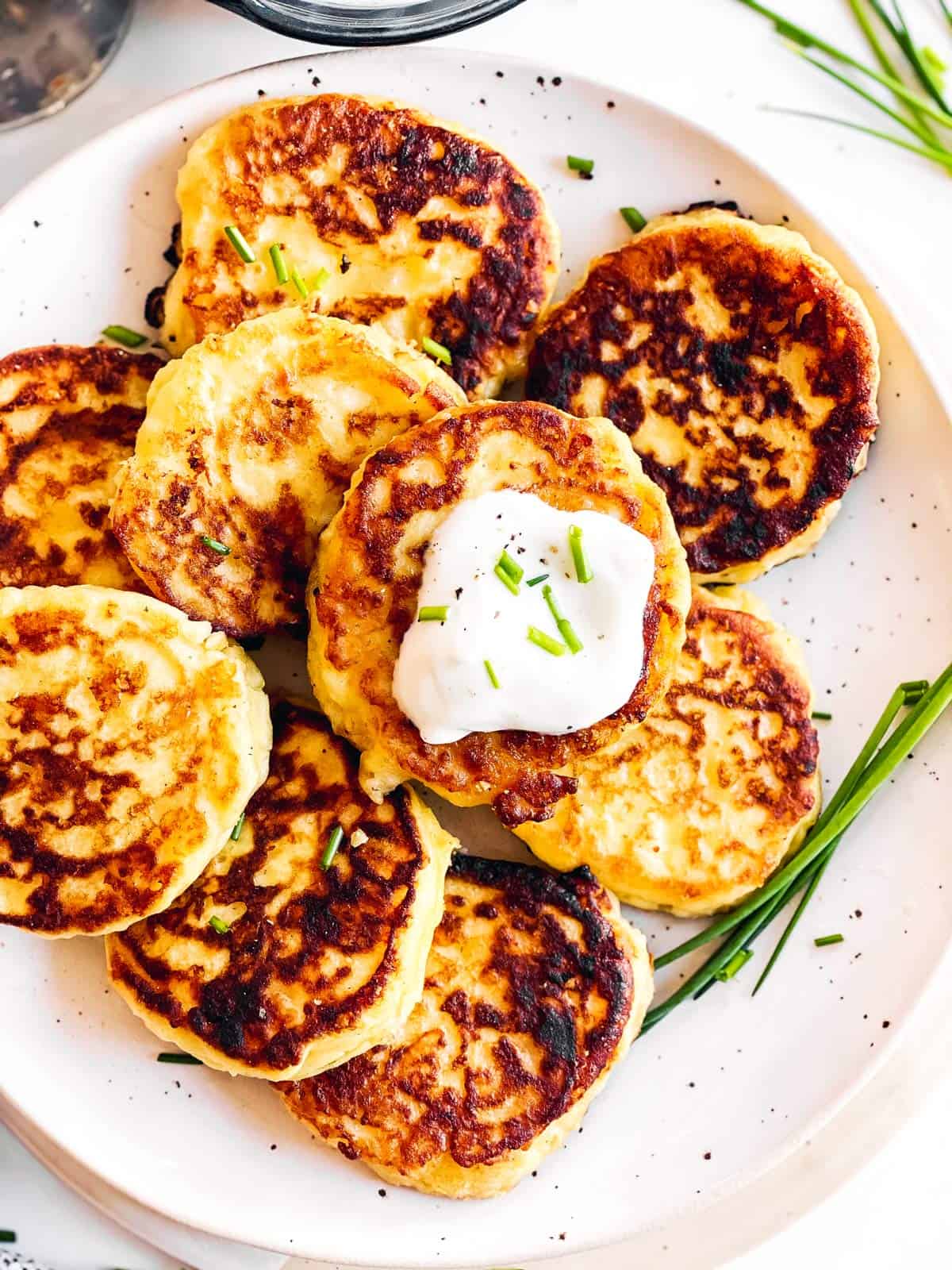 overhead close up view of potato pancakes on white plate with sour cream