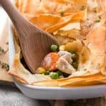 turkey pot pie in white casserole dish with wooden spoon sticking in filling