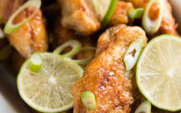 white enamel dish filled with crispy chicken wings, lime slices and chopped green onion on pink napkin
