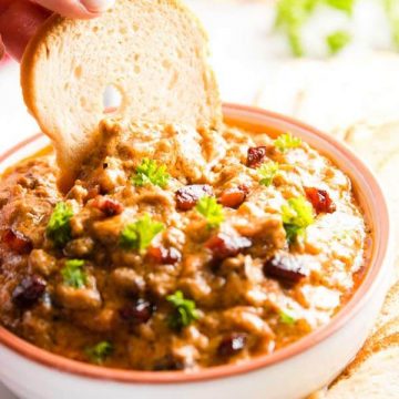 dipping a bread chip into a bowl with crock pot bbq bacon cheeseburger dip