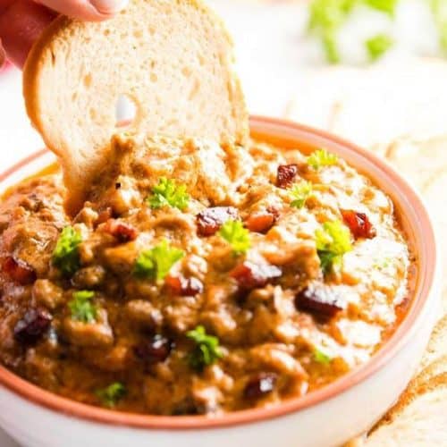 dipping a bread chip into a bowl with crock pot bbq bacon cheeseburger dip