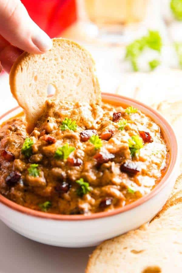 dipping a bread chip into a bowl with crock pot bbq bacon cheeseburger dip