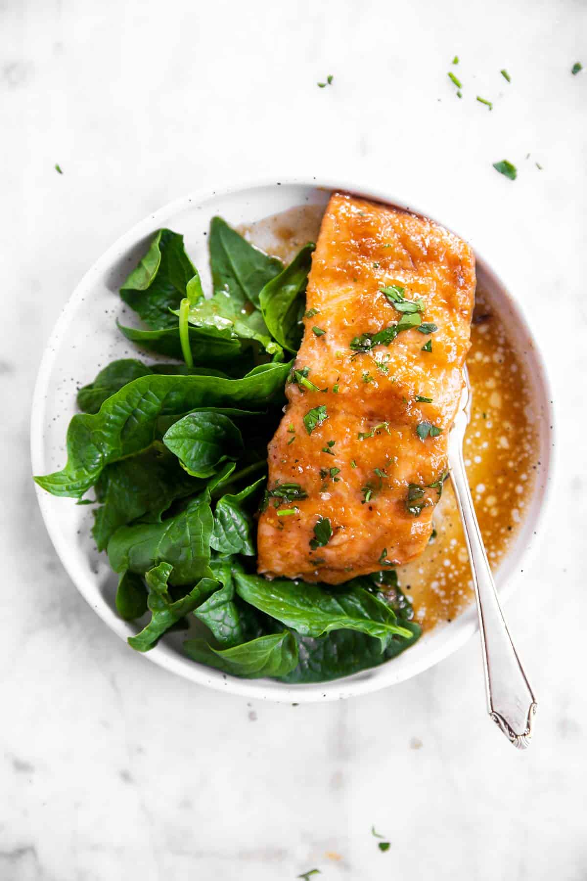 white plate with honey garlic baked salmon and spinach on white marble surface