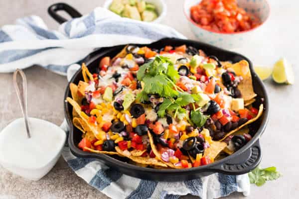 vegetarian nachos in black skillet surrounded by small bowls with nacho toppings