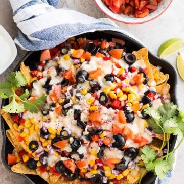 top down view on black cast iron skillet with vegetarian nachos next to bowls with avocado and salsa