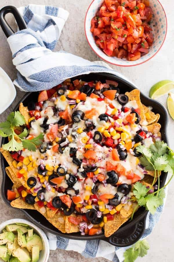 top down view on black cast iron skillet with vegetarian nachos next to bowls with avocado and salsa