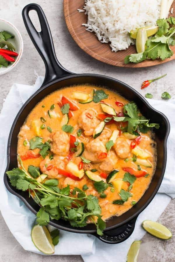 top down view on cast iron skillet with Thai shrimp curry next to wooden platter with rice