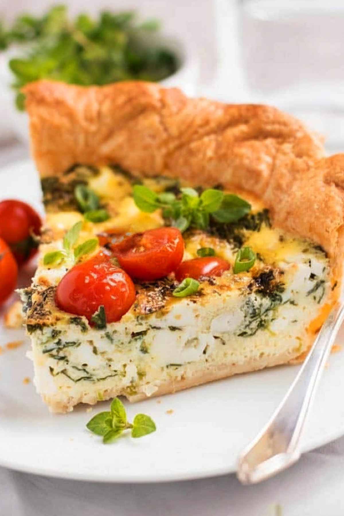 Slice of tomato spinach feta quiche on plate.